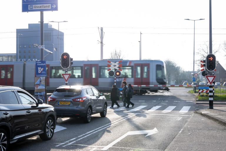 Auto's op de Kralingseweg wachten voor de spoorwegovergang terwijl een metro passeert